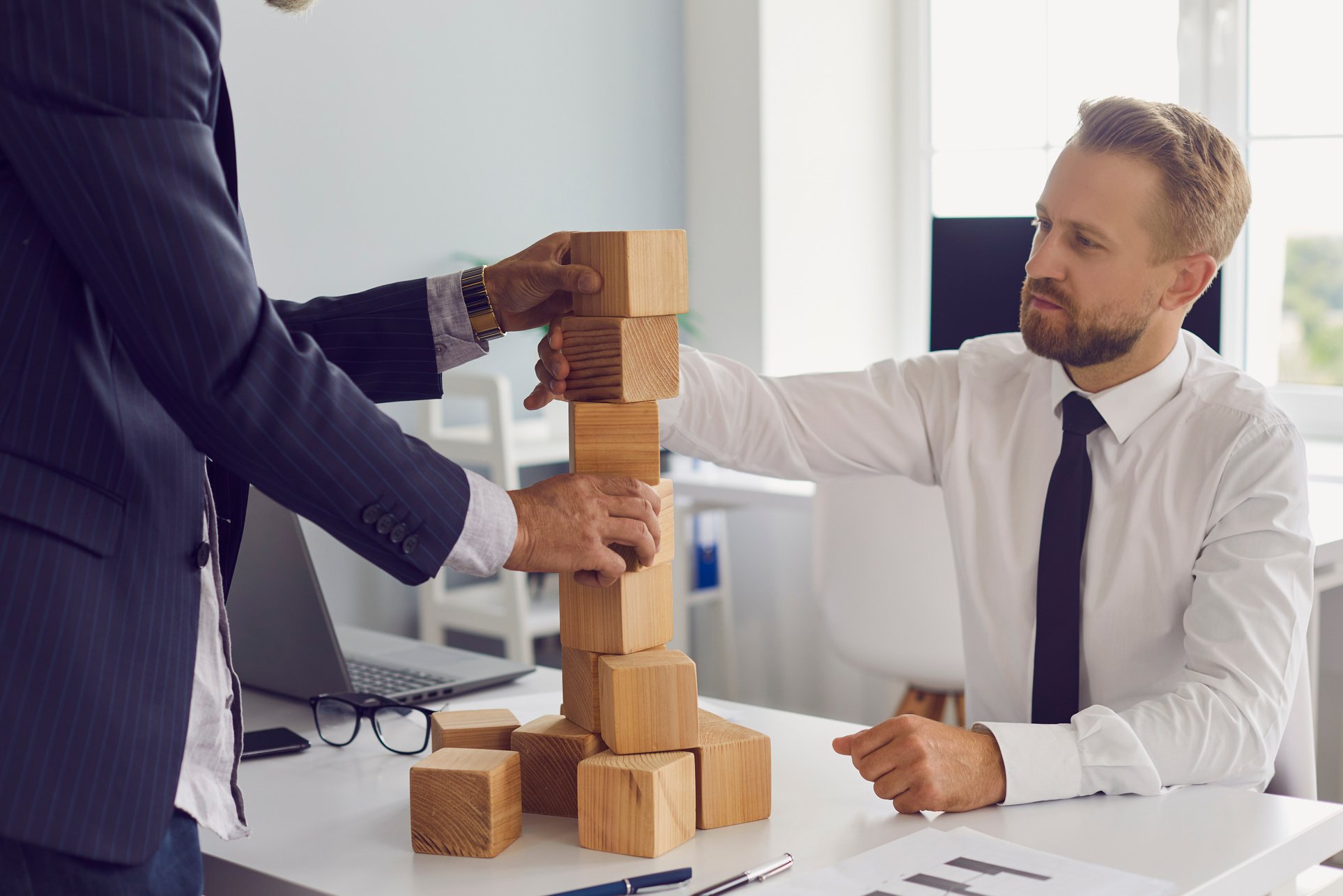 Partners Building Tower of Wooden Blocks on Office Table Together Developing Strategy for Business.